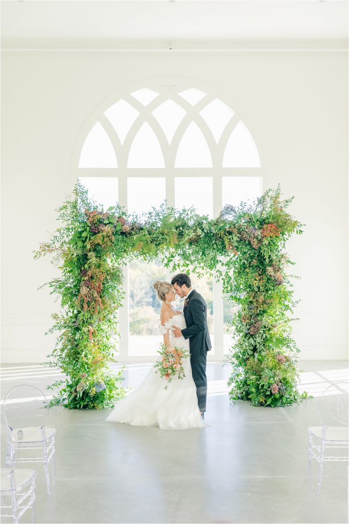 Bride and groom in from of green ceremony arched at Westwind Hills Westwind Hills ceremony with arched windows and greenery at alter Westwind Hills luxury wedding inspiration | Kelsey Alumbaugh Photography | #weddinginspiration #luxurywedding #stlouisweddingphotography #stlwedding #styledshootsacrossamerica