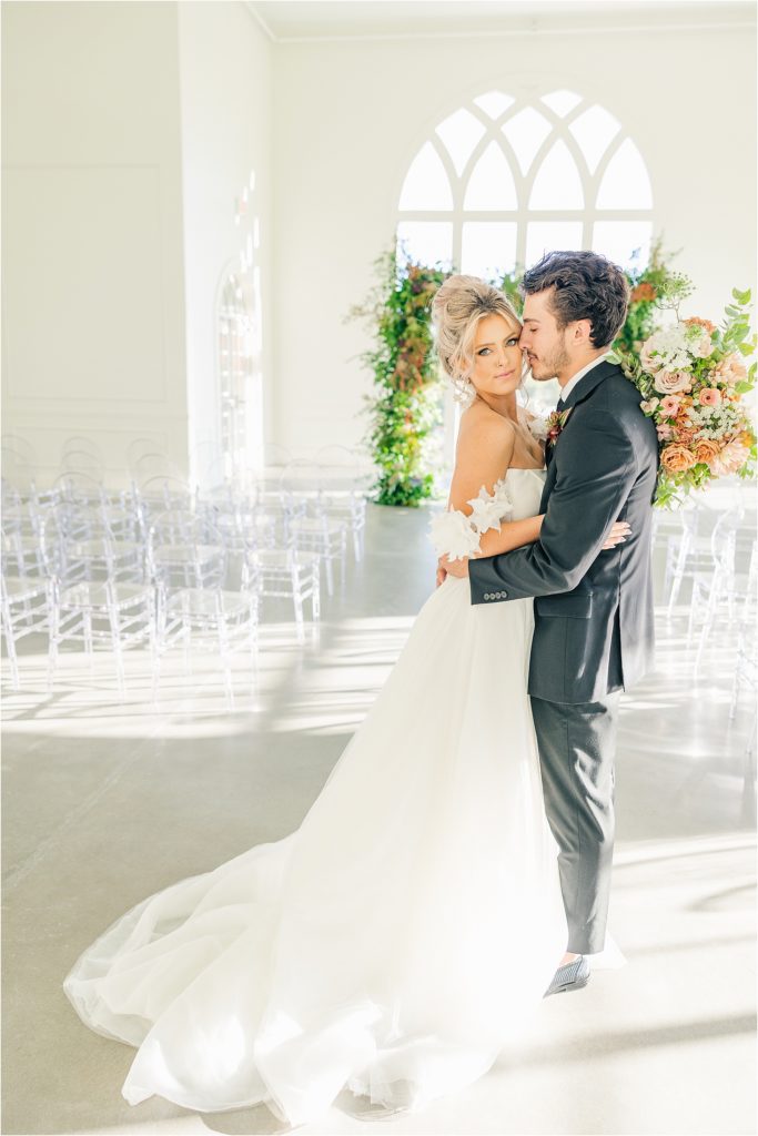 Bride in white off the shoulder wedding gown with groom in black tux nuzzled in and smiling Westwind Hills luxury wedding inspiration | Kelsey Alumbaugh Photography | #weddinginspiration #luxurywedding #stlouisweddingphotography #stlwedding #styledshootsacrossamerica