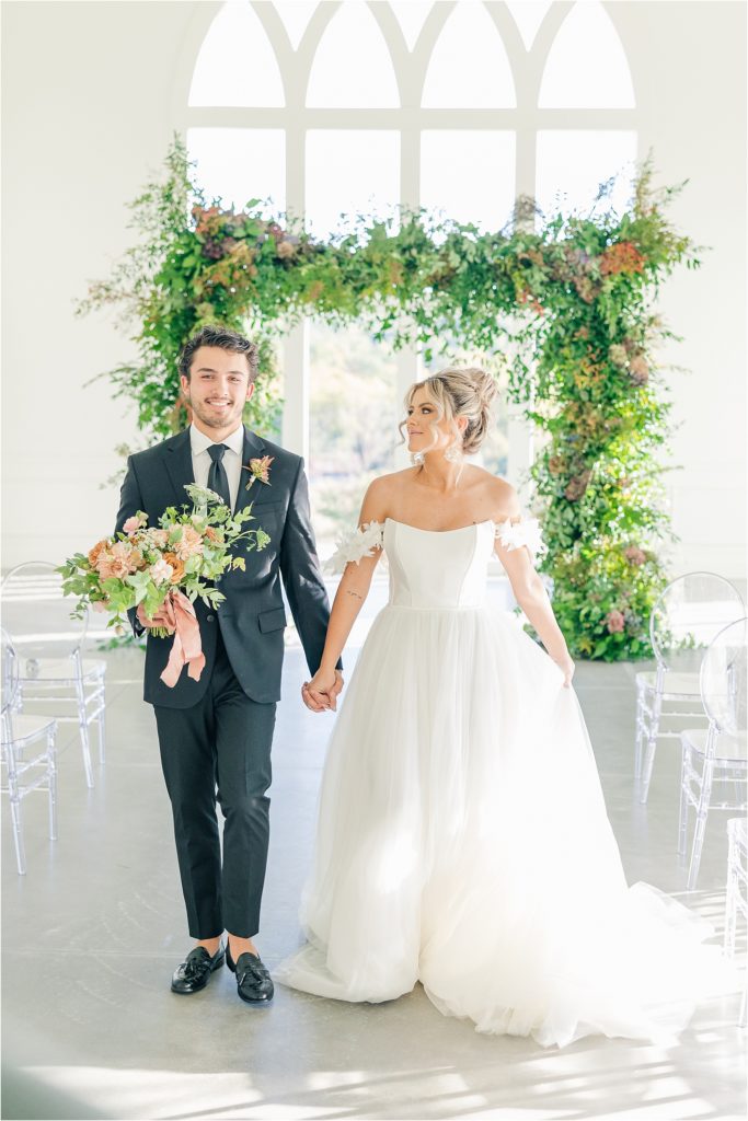 bride in off the shoulder white wedding gown and groom in black tux in aisle at Westwind Hills luxury wedding inspiration | Kelsey Alumbaugh Photography | #weddinginspiration #luxurywedding #stlouisweddingphotography #stlwedding #styledshootsacrossamerica