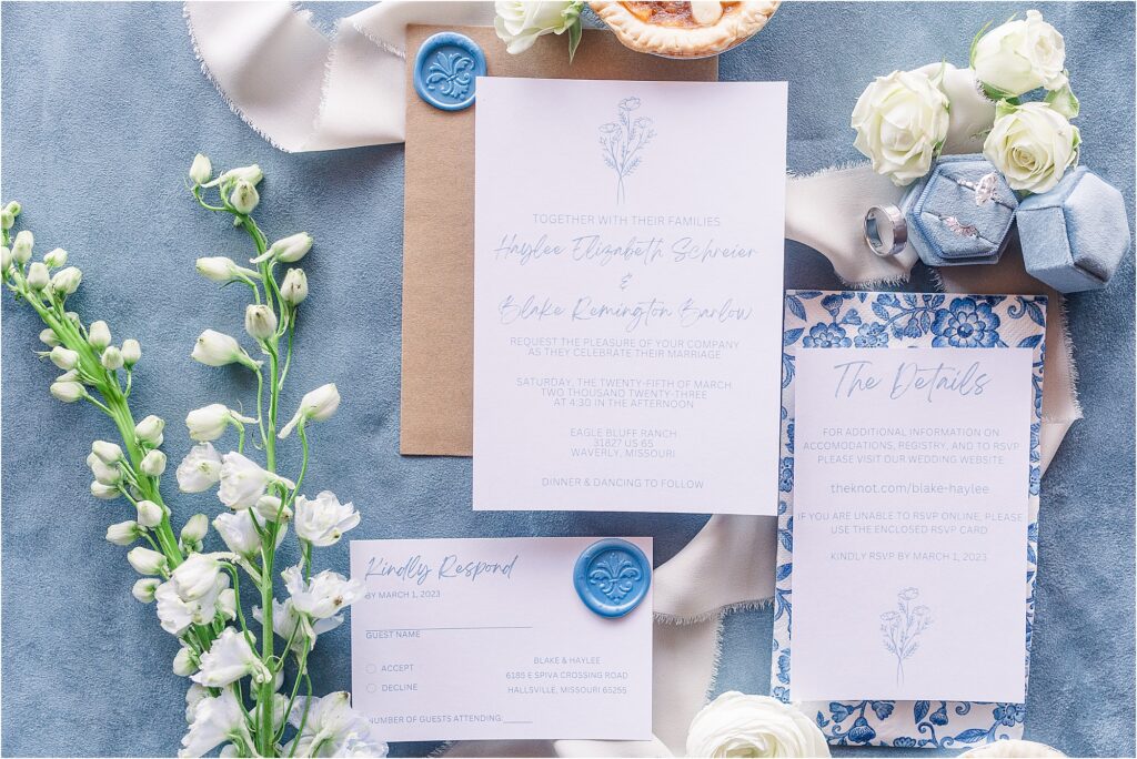 White wedding invitations on blue background with florals, rings in blue velvet ring box and tiny apple pies Haylee + Blake | Missouri River spring wedding | Kansas City wedding photographer | Kelsey Alumbaugh Photogrpahy | #kansascitywedding #missouriweddingphotographer #missourispringwedding 